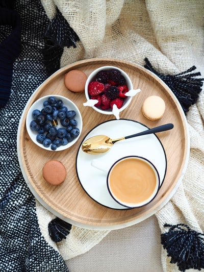 一杯咖啡放在碗上的覆盆子和蓝莓旁边的平面摄影